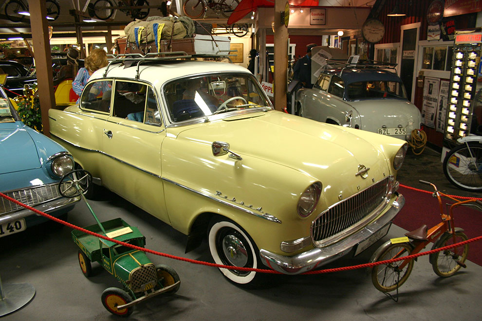 Längst till vänster skymtar en 1961 Ford Anglia 106E. Modellen som hade ”felvänd” bakruta. Den gula bilen är en 1957 Opel Rekord och till höger skymtar bakpartiet av muséets 1956 Lloyd LP400S. Glöm inte att beskåda den otroliga lilla lastbilen med ratt och styrning, som en lycklig gosse en gång i tiden kunde framföra, genom att promenera bakom fordonet!
