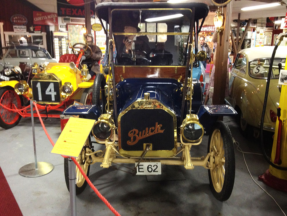 Vilken lyx med mörkblå lackering och matchande beige randning, toppat med massvis av glänsande mässing! Bilen är en 1910 Buick Roadster. Till vänster syns fronten på 1912 Ford Model T Speedster.