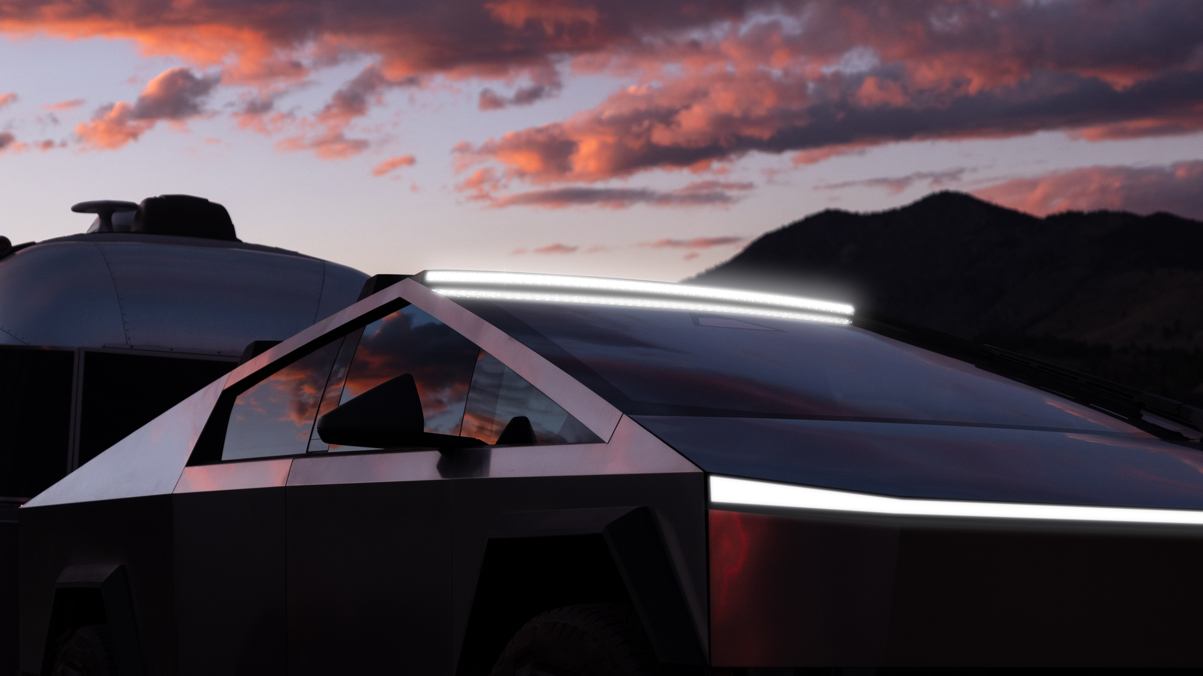 Sidan av en Tesla Cybertruck med reflekterande fönster, ett tak med ljusramp och en baklykta mot en himmel med solnedgång.