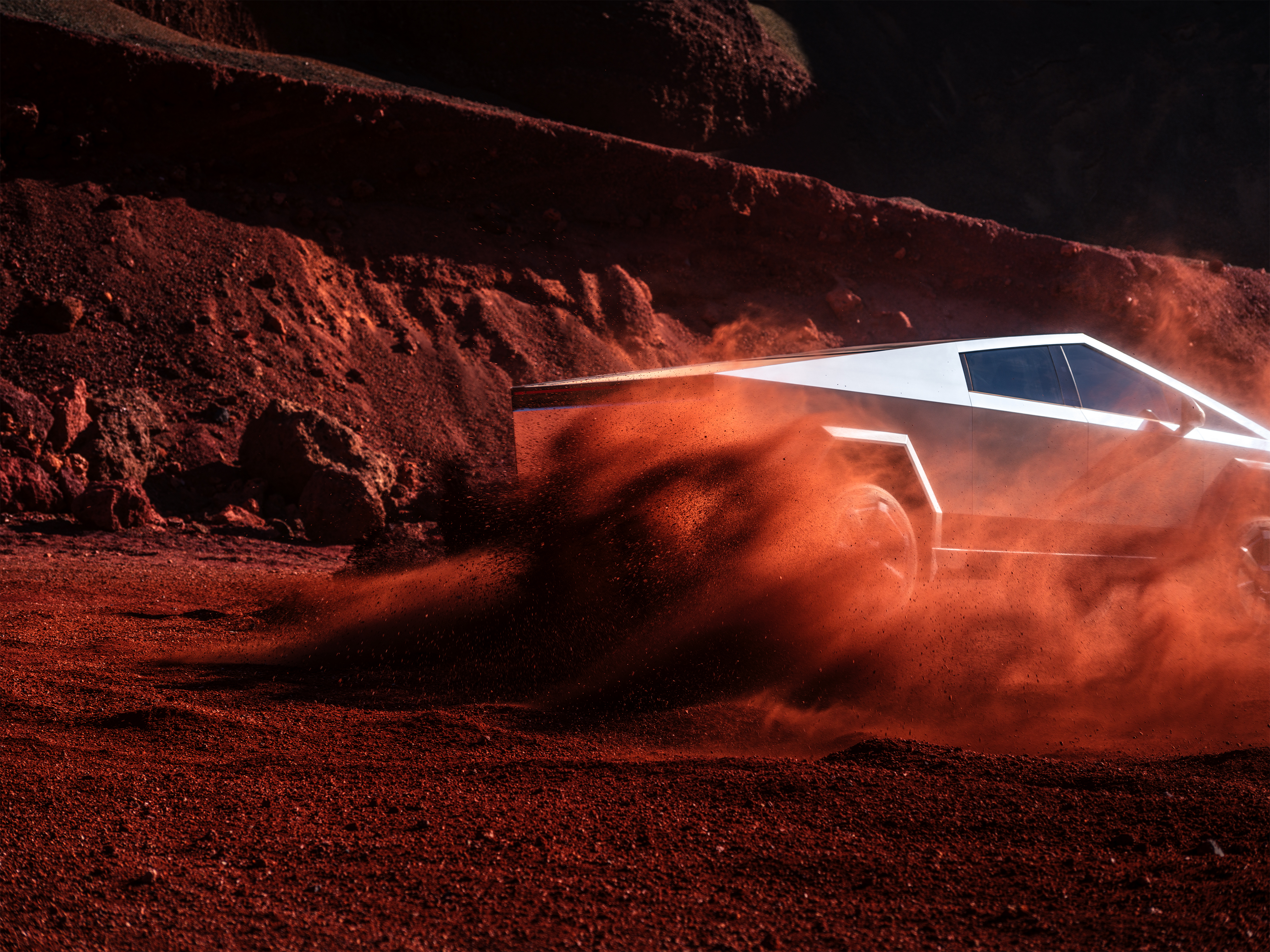 Tesla Cybertrucks sidolucka, förmodligen täckt i grus, med en rödbrun grusmiljö som bakgrund där solljuset reflekteras.