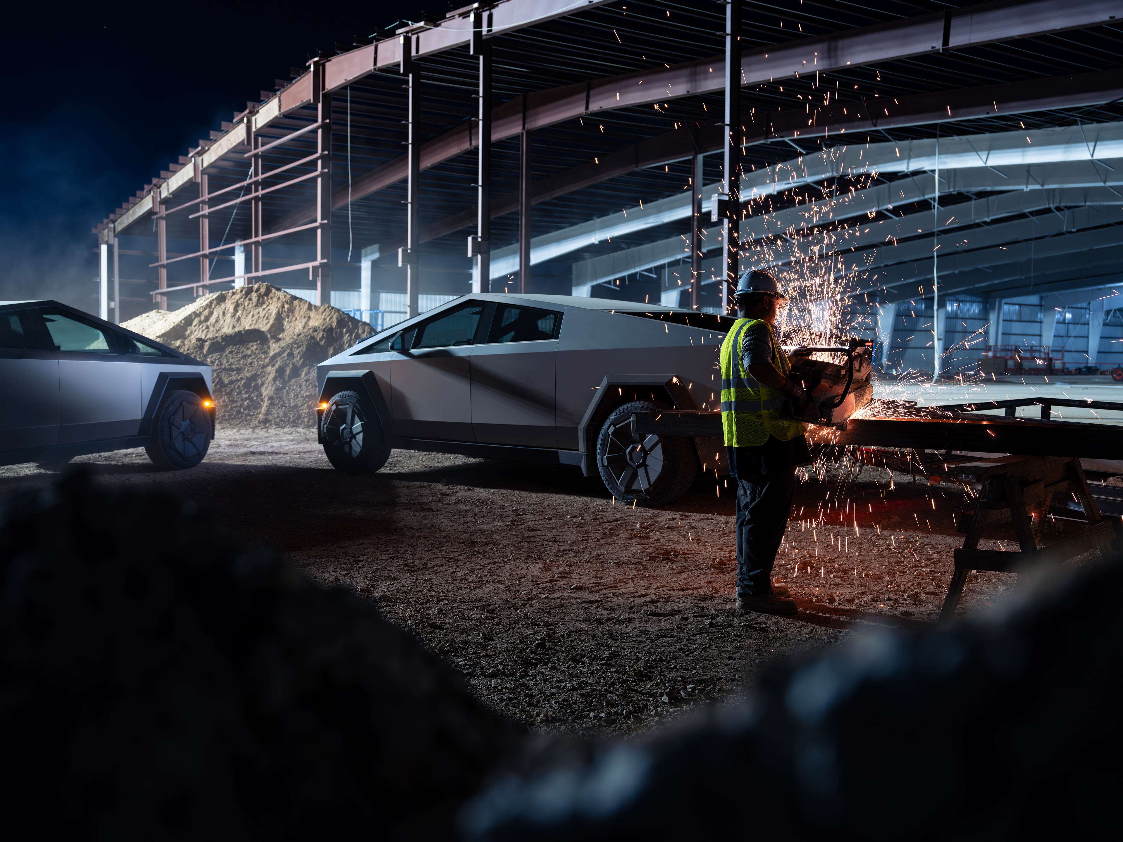 En Tesla Cybertruck står på grus, gnistor flyger runt dess högra sida och fälgen. Stålkonstruktioner i bakgrunden.
