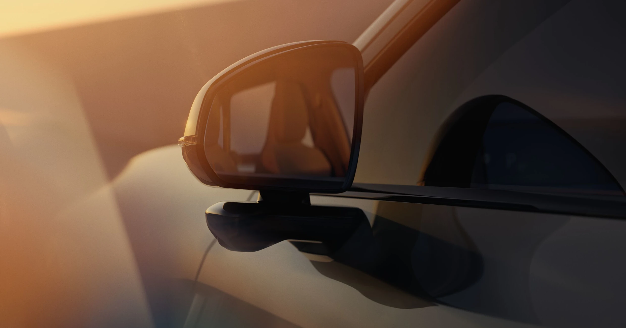 En närbild av sidospegeln på Volvo EX60 som visar en slimmad design med integrerad kamera under solnedgångens varma ljus.