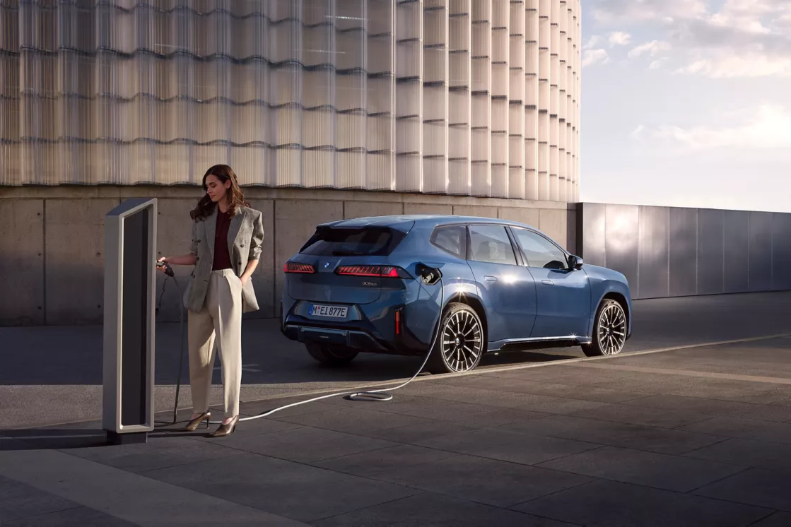 BMW iX3 har en ny generation battericeller som ger ultrasnabb laddning. Bilden visar en kvinna ansluta laddkabeln till fordonet.