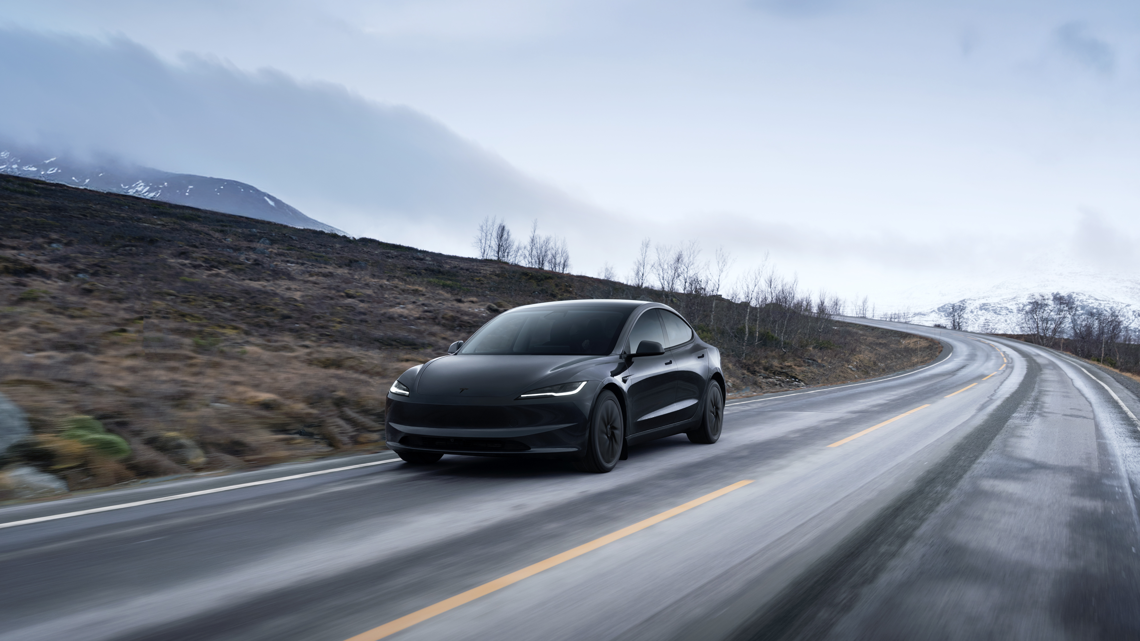En Tesla Model 3 Long Range kör på en slingrande landsväg med snöklädda berg i bakgrunden. Modellen kom 2019 och var en milstolpe för elbilar.