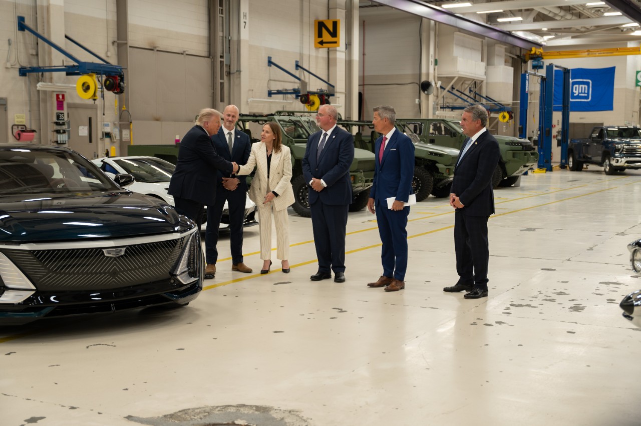 Trump under ett besök i GM:s fabrik, där han skakar hand med en av de anställda. I bakgrunden ses bland annat en Cadillac Celestiq