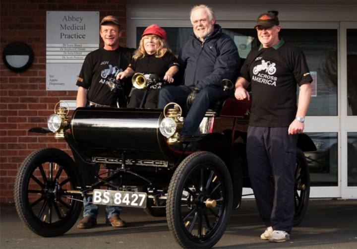 Bilen är en Oldsmobile Curved Dash Model 6C. Bakom ratten sitter Joy Rainey. Till vänster om henne har vi Mark Riley, flankerade av Jim Carr och Nick Cooper.