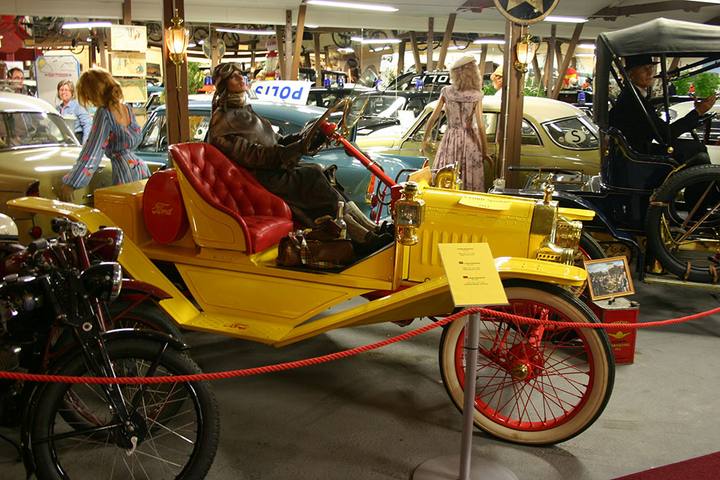 Ett myller av bilar, välklädda skyltdockor och annan automobilia. I förgrunden en knallgul 1912 Ford Model T Speedster med röd läderklädsel.