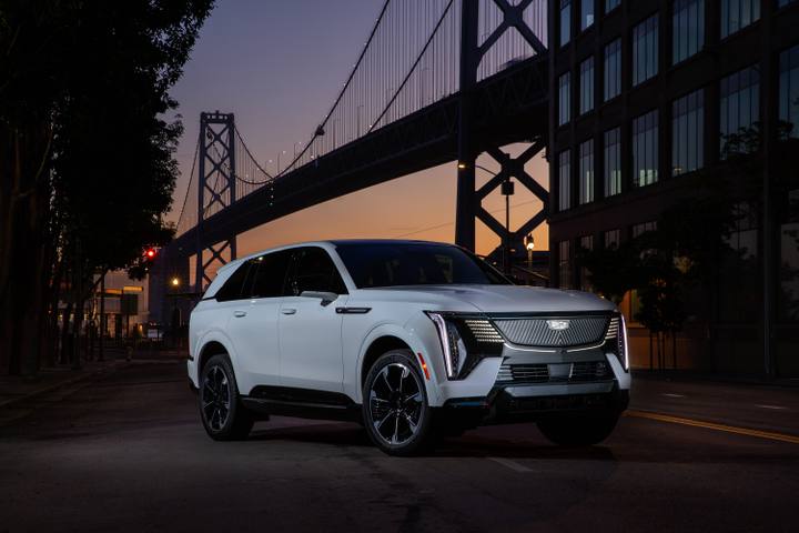 Cadillac Escalade IQ visar upp sin imponerande front och upplysta grill mot en dramatisk kvällshimmel med en bro i bakgrunden.