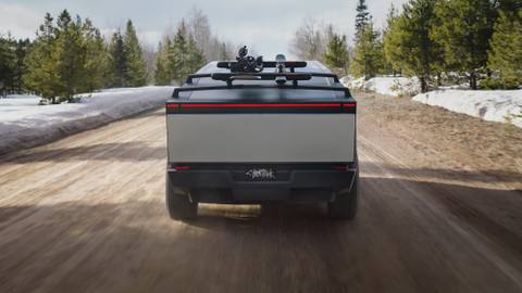 Cybertruck med takräcke för vinterutrustning på en snöig skogsväg. Den breda bakljusrampen är ett tydligt signum.