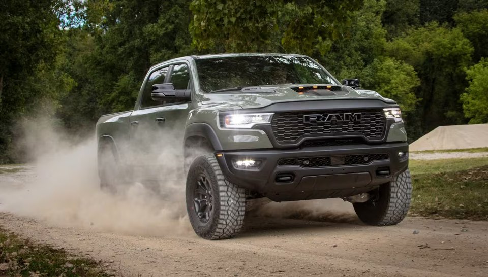 En grön Ram 1500 Rebel kör på en grusväg med damm virvlande runt däcken. Modellen är känd för sin terrängförmåga och aggressiva design.