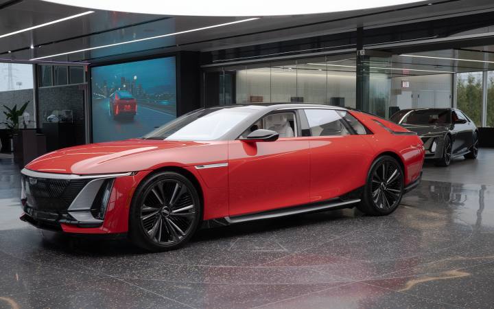 Den röda Cadillac Celestiq visas upp i en studio. Bakom skymtar en mörkare modell och en stor skärm som visar bilen i rörelse.