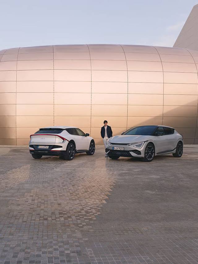 Kia EV6 har en futuristisk design som signalerar Kias nya inriktning. Här i två färger, flankerade av en person.