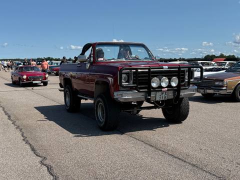 En imponerande Chevrolet K5 Blazer rullar fram p% flygf%ltet, med en Volvo P1800 i bakgrunden. En klassisk syn fr%n Big Swap Meet i Lidk%ping.