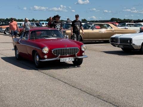 En röd Volvo P1800 rullar sakta fram på Hovby flygfält. Denna klassiska svensk bland de amerikanska veteranbilarna lockade många blickar.